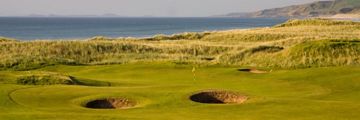 A view of Machrihanish Golf Club in Kintyre on the west of Scotland with a green surrounded by classic links pot hole bunkers