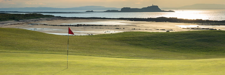 Looking across the green of the 17th hole at North Berwick West Links over the beach to the island of Fidra and the hills of Fife in the distance.